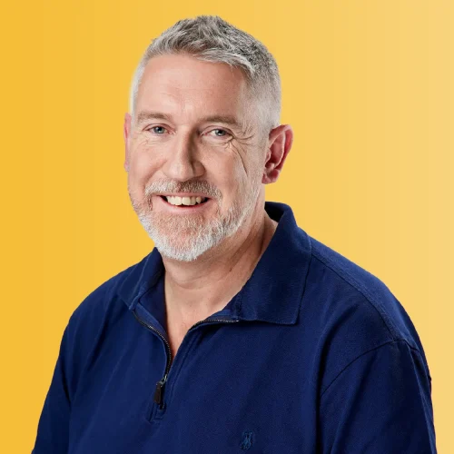 Image of Male, Andrew Lammiman, Head of Product Engineering. Man in image with short facial hair, smiling at camera in navy zipped polo shirt against a yellow gradient background.