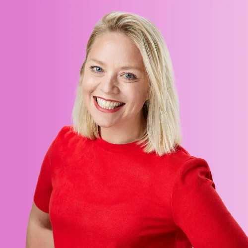 Image of Female, Ceri Pritchard, Head of HR. Wearing a red, mid-sleeve dress, smiling at the camera against a pink gradient background.