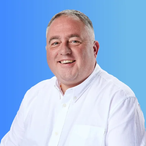 Image of Male, Nigel Smith, Head of Professional Services. Wearing white shirt, and smiling into the camera against a blue gradient background.